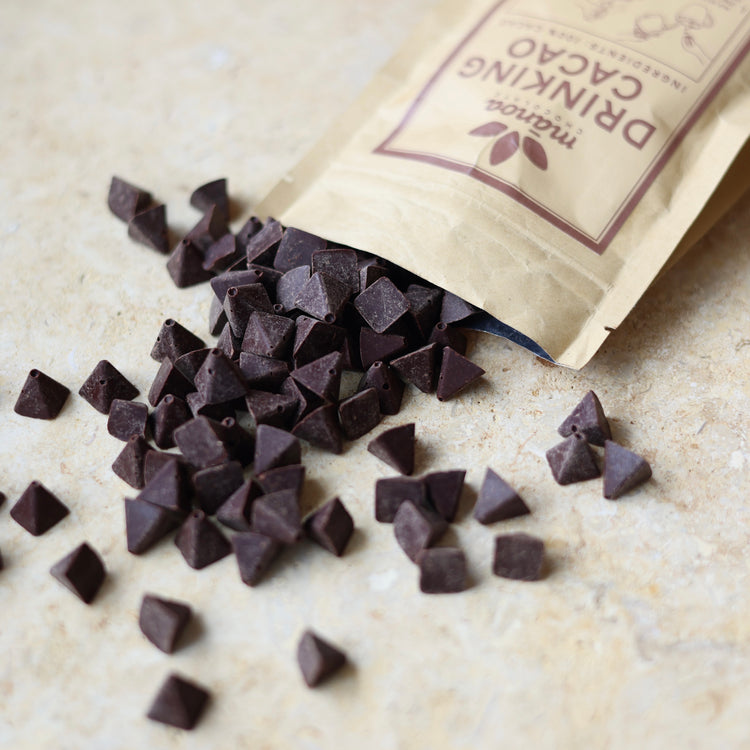 Image of a pouch of Manoa Drinking Cacao with scattered cacao pieces in front