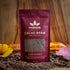 Image of an 8oz bag of Cacao Brew with cacao brew, cacao beans, tropical flowers and cacao pods on a wooden table
