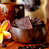 Image of chocolate squares covered in cacao nibs, sitting in a wooden bowl