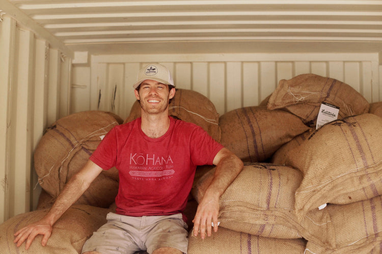 Image of man sitting on burlap bags filled with cacao beans