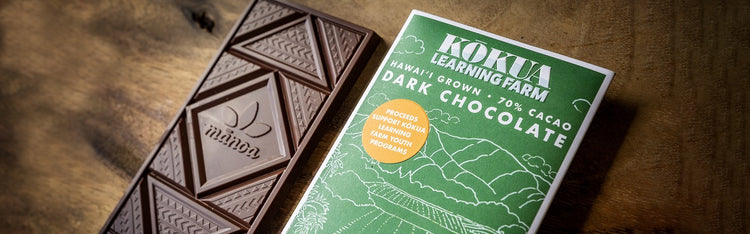 Dark chocolate bar with geometric patterns and a green Kokua Learning Farm packaging on a wooden surface.