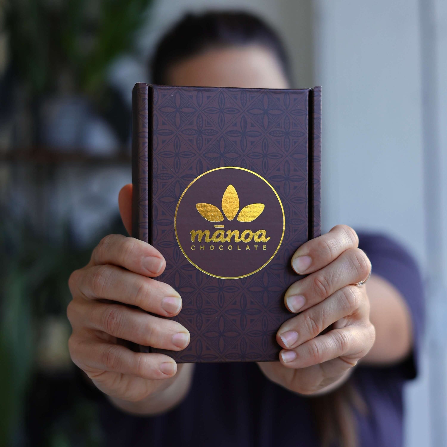 Image of person holding box of chocolate with gold Manoa logo