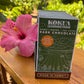 Image of a box of Kokua Learning Farm dark chocolate with a pink flower on a wooden surface
