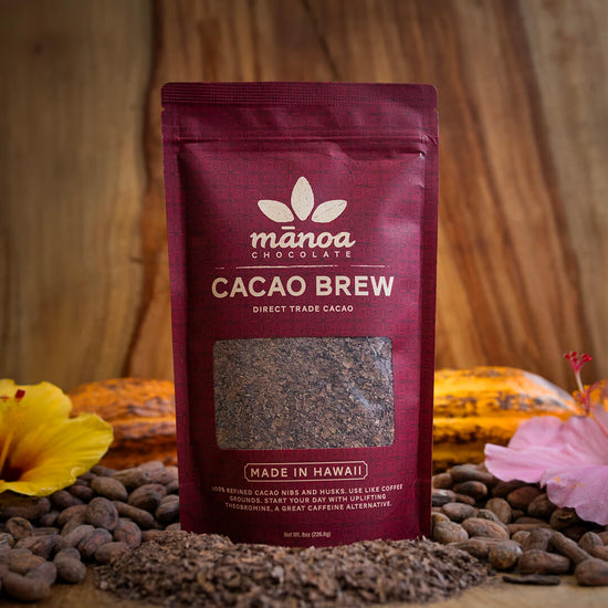 Image of an 8oz bag of Cacao Brew with cacao brew, cacao beans, tropical flowers and cacao pods on a wooden table