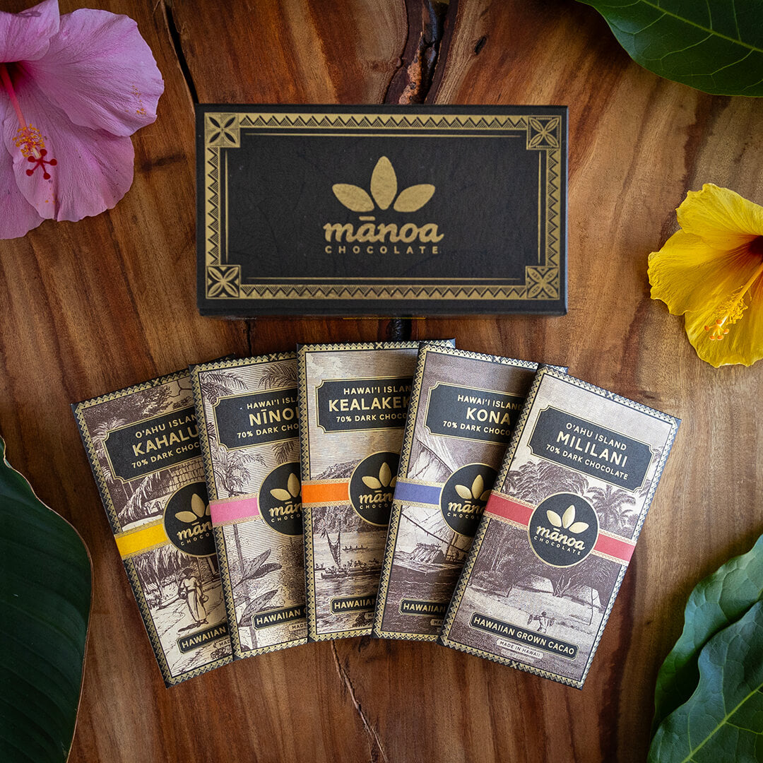 Image of 5 Hawaii grown chocolate bars packaged with gift box on wooden table with tropical plants as garnish