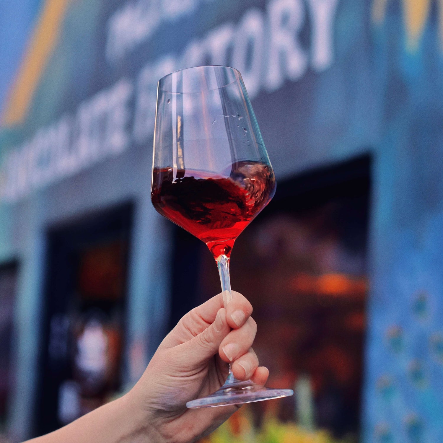 Image of hand holding wine glass in front of Mānoa Chocolate storefront