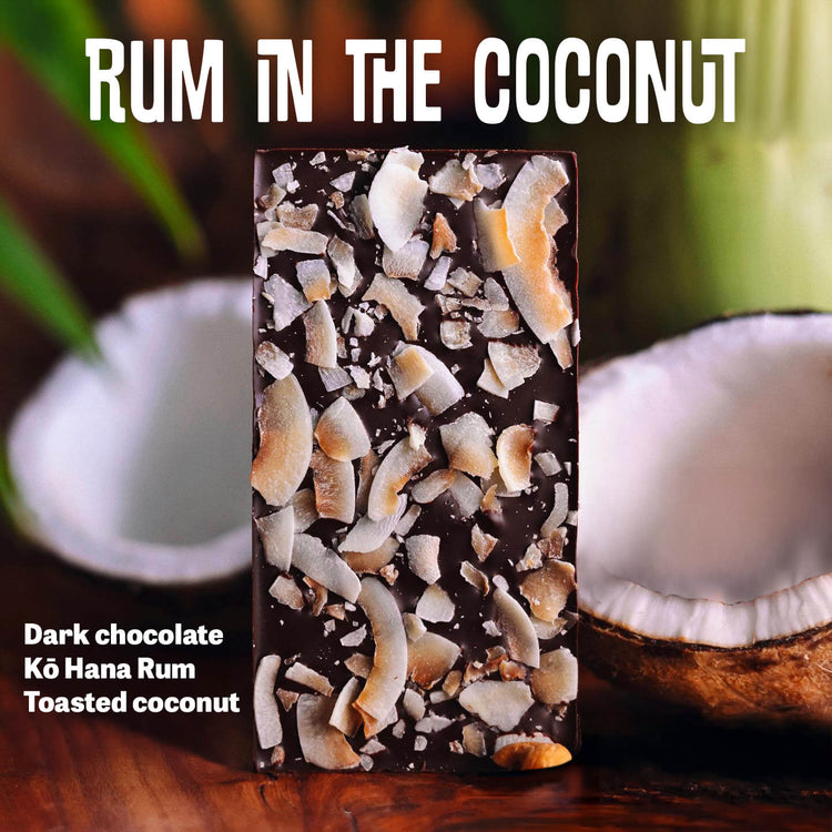 Image of chocolate bar sprinkled with toasted coconut with halved coconuts in the background; title text reading: Rum In The Coconut; description reading: Dark Chocolate, Ko Hana Rum, Toasted Coconut