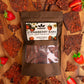 Image of Strawberry Bark Dark Chocolate package surrounded by Strawberry Bark pieces and freshly cut strawberries on table.