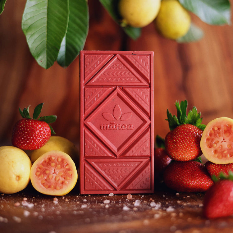 a pink strawberry guava chocolate bar on a wooden table with fresh strawberries, guava fruit, and salt