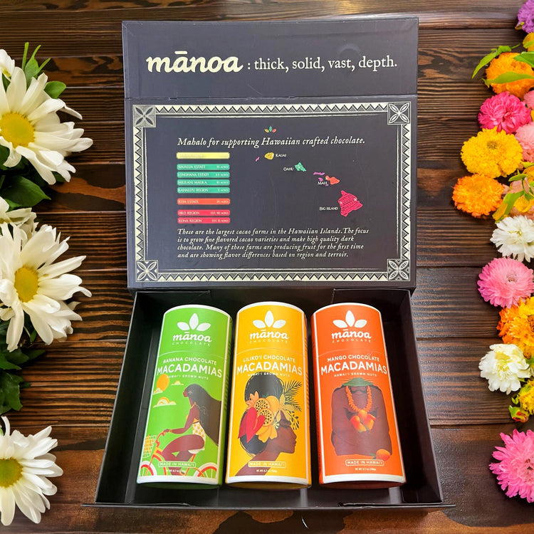 Image of mango, lilikoi, and banana macadamia nut tubes with black and gold manoa-branded treasure box