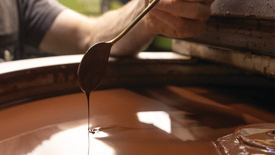 image of spoon dipped in chocolate drizzling over a vat of molten chocolate