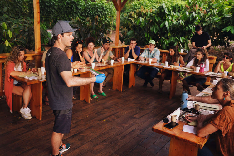 Image of a man giving a group of guests a chocolate tasting in a cacao orchard