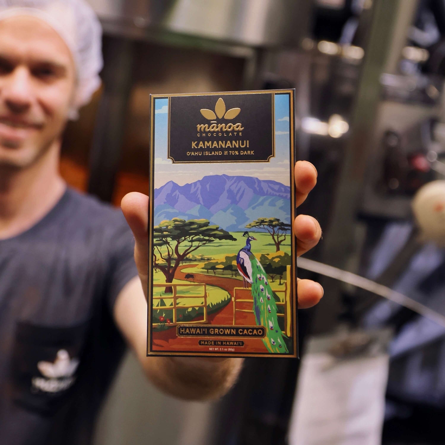 Image of chocolate maker holding Kamananui package with machines in background