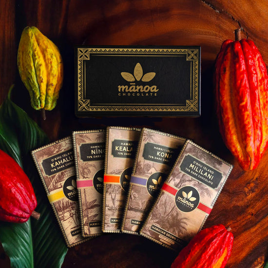 Image of 5 Hawaii grown chocolate bars packaged with gift box on wooden table with tropical plants as garnish