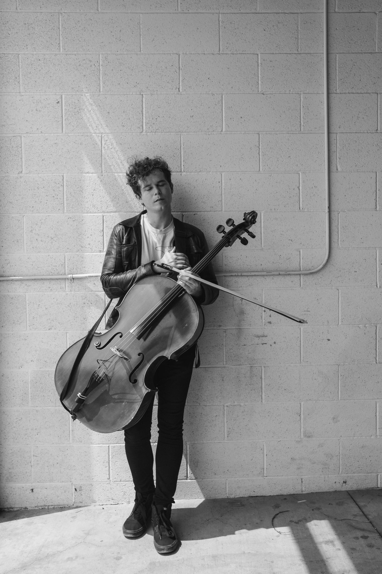 Black and white image of musician LoveJack holding a cello and leaning against a wall