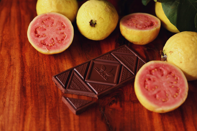 a guava dark chocolate bar on a wooden table with fresh guava fruit laying around it