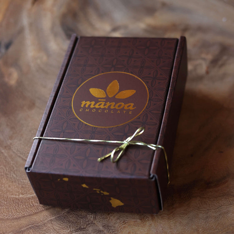 Manoa Chocolate packaging with a gold bow on a wooden surface