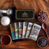 Image of 6 chocolate bars sitting among a gift box, cacao beans, sugar and nibs