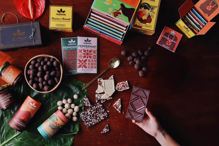 Assorted chocolate bars, gift boxes, chocolate macadamias and packaging on a wooden surface