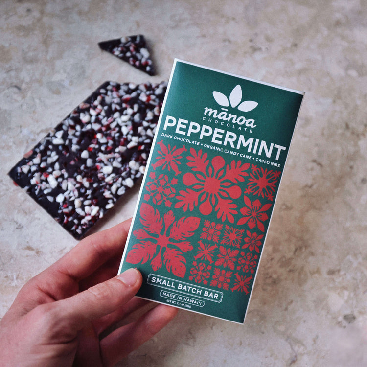 image of Manoa Chocolate peppermint crunch dark bar packaging held by a hand over a textured  white surface