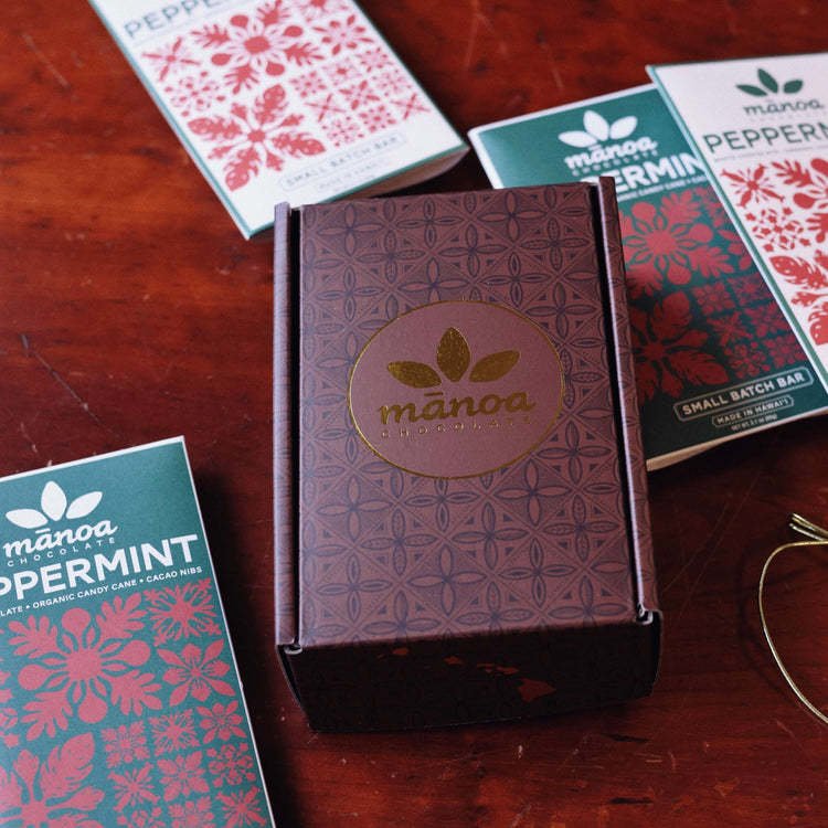 image of manoa chocolate brown 4 bar  box on a wooden table with peppermint chocolate bar packages around it