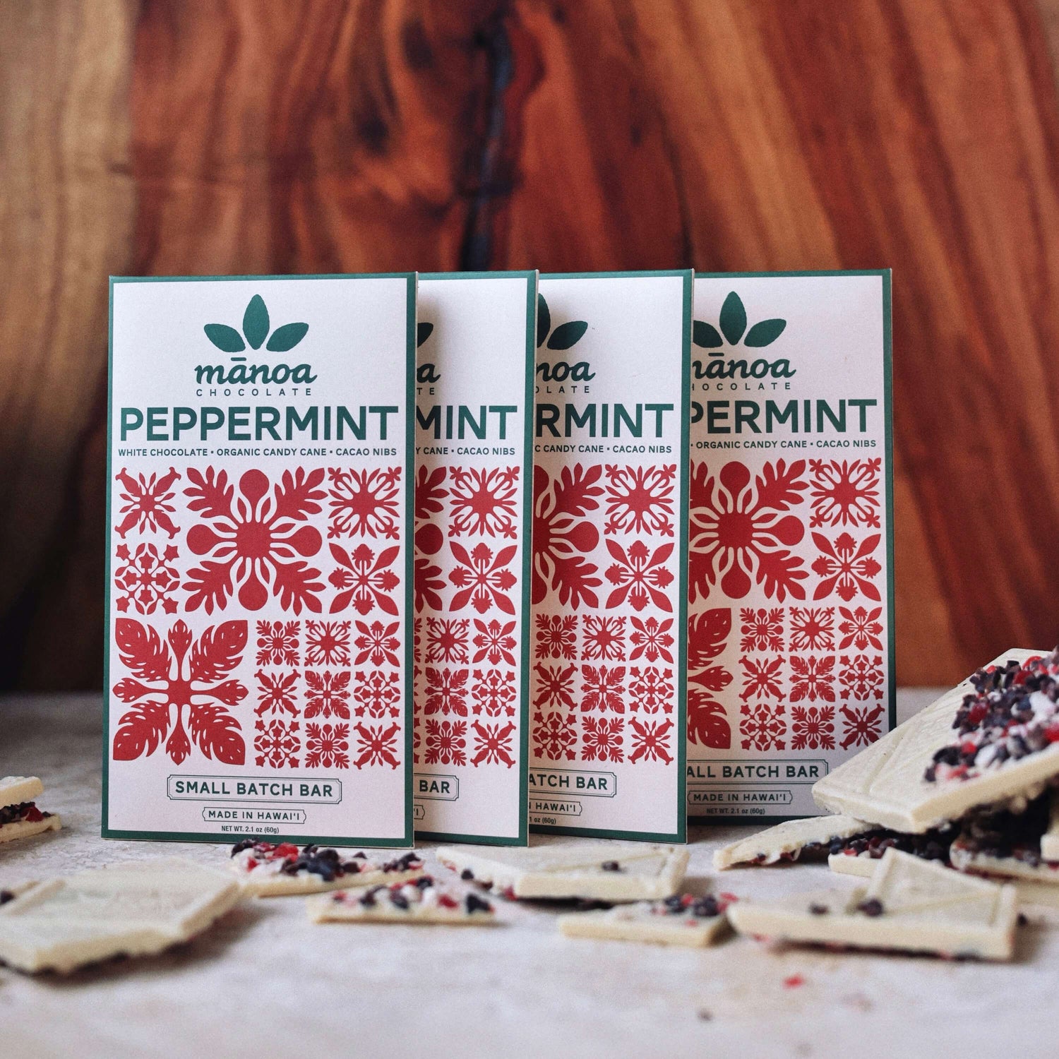 image of four packages of white Manoa Chocolate Peppermint crunch bars on a wooden surface with some bars visible.