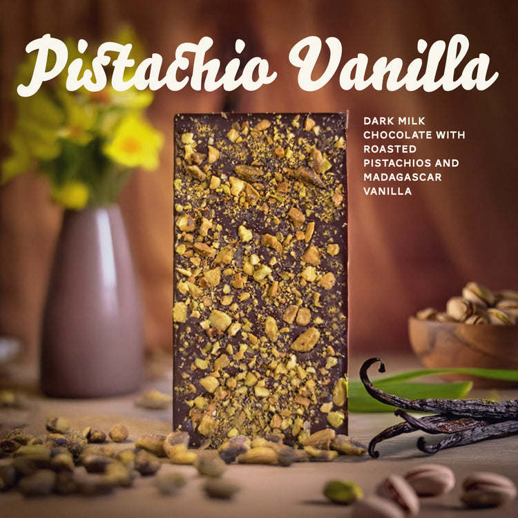 a chocolate bar covered with crushed pistachios with Hawaiian plants garnishing the background, a Manoa Chocolate logo and text reading Pistachio Vanilla: dark milk chocolate with roasted pistachios and Madagascar vanilla