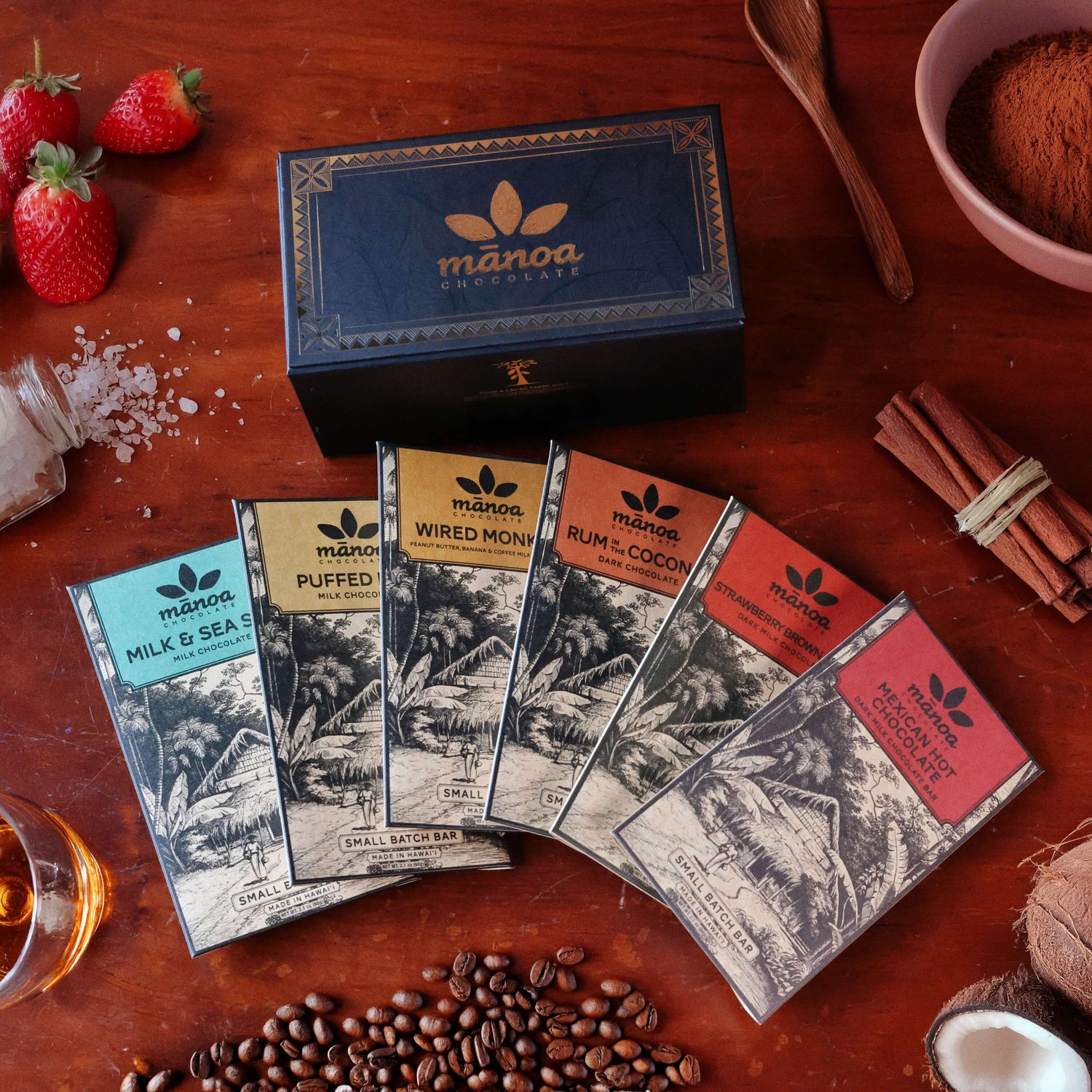 Manoa chocolate bars on a wooden surface with strawberries, coffee beans, and spices.