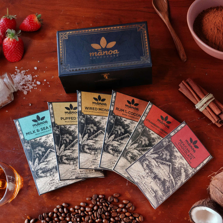 Manoa chocolate bars on a wooden surface with strawberries, coffee beans, and spices.