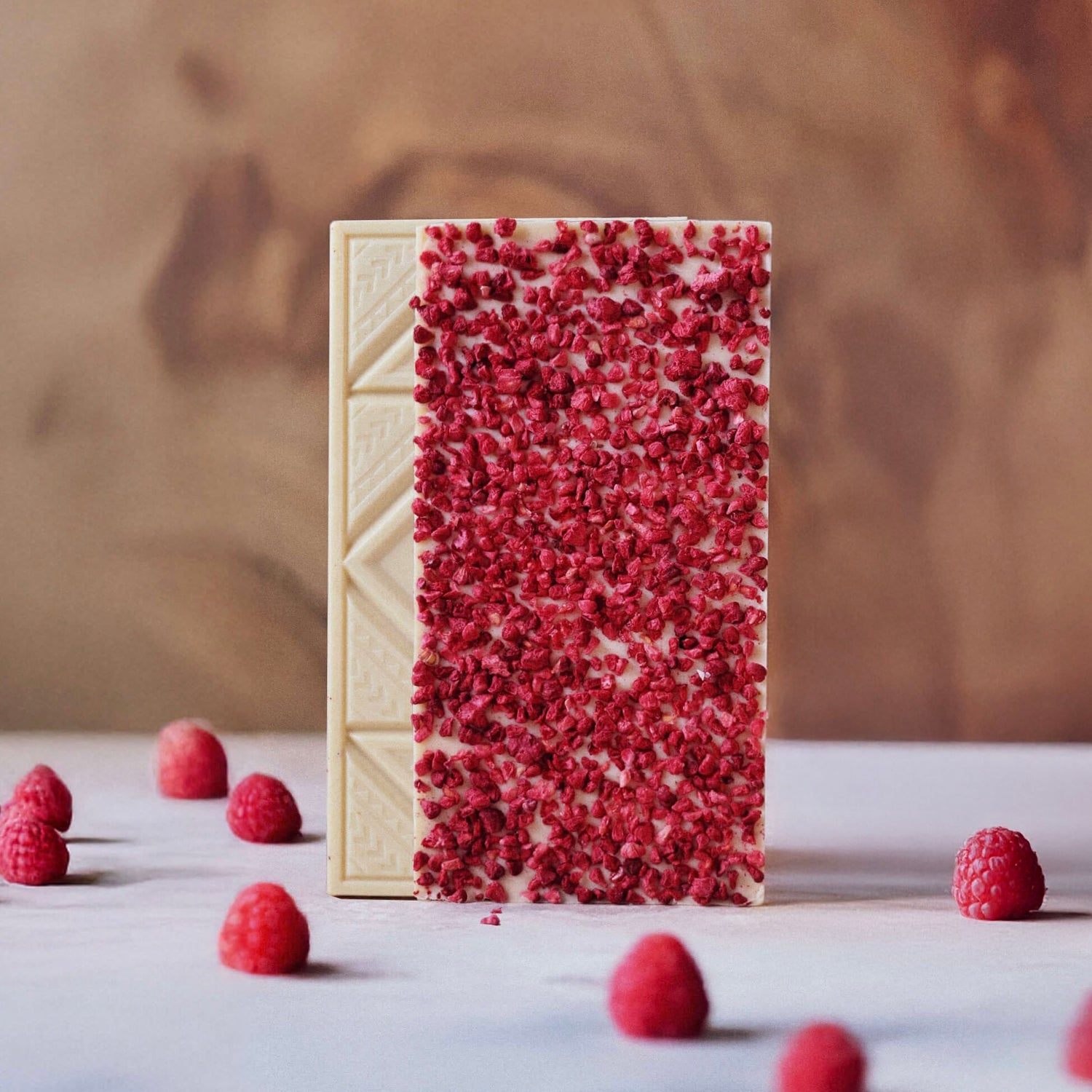 white raspberry chocolate bars on a marble surface with raspberries surrounding them