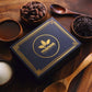 Image of gift box with gold Manoa logo sitting among cacao beans, nibs and sugar